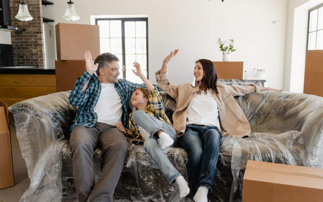 A family is sitting on a couch surrounded by moving boxes in their new custom home in Southern Utah Valley.